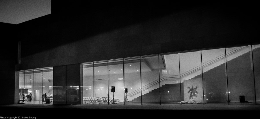 The Nerman after the performance of Relic by Jonah Bokaer with the after-reception crowd just showing in the left window and the audience space and set showing in the right window with the Relic standing in front of the stairs